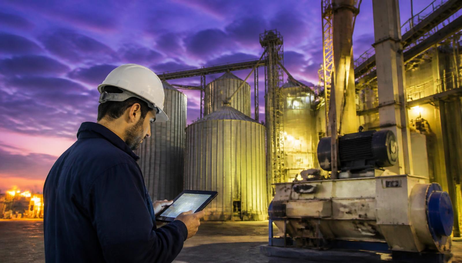 Feed mill engineer reviewing an automated capacity and ROI calculation on a tablet beside grain silos